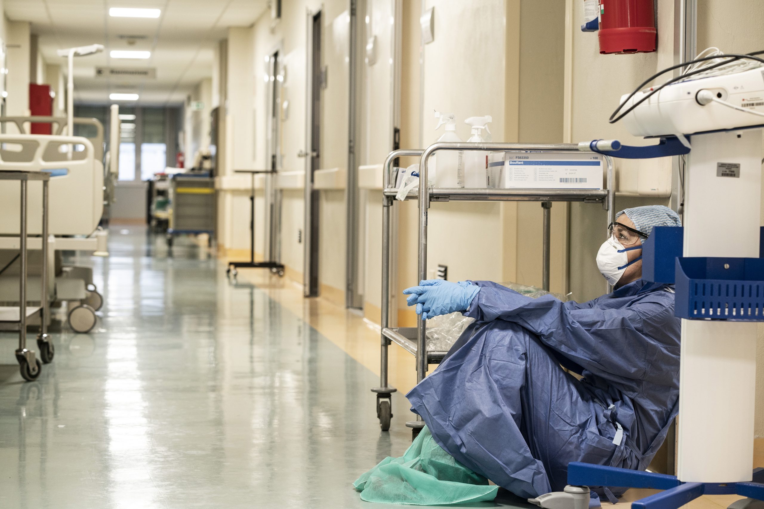 Photo of a person in scrubs slumped down at the end of an empty hospital corridor - licensed under Creative Commons